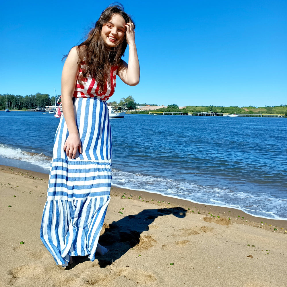 model is on the beach wearing a blue and red striped dress.