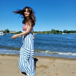 Brunette model is wearing a red and blue stripped dress on a beach.