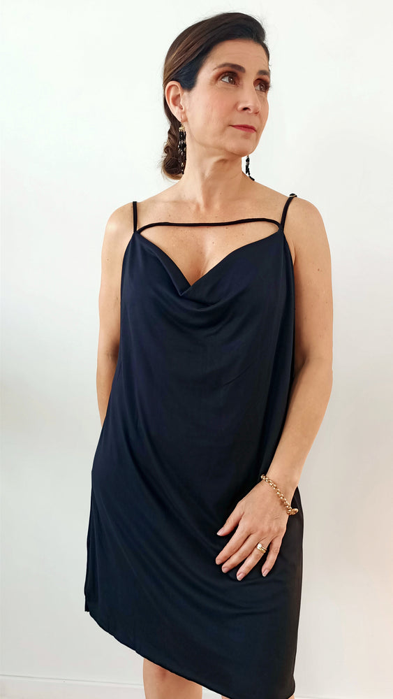 model wears basic black dress in cotton, draped at the chest.