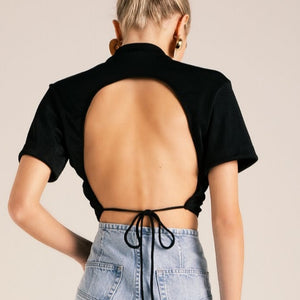 
                  
                    Blond model wears a cropped open back black top that is tied with a thin stripe. Bottom is a jeans pants
                  
                