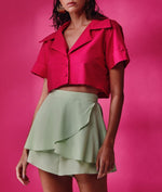 Brunette model wears a cropped pink short sleeved top and pastel green short-skirt